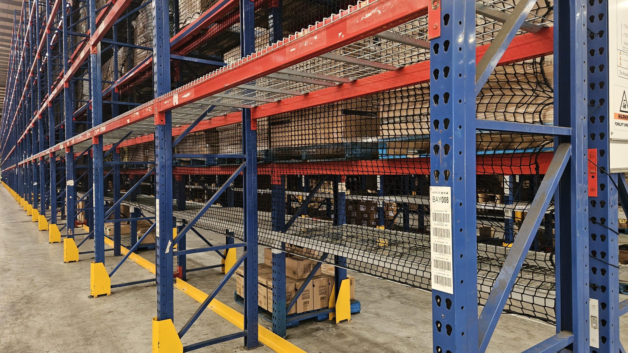 Pallet rack netting installed across blue and orange warehouse racking
